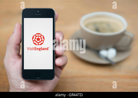 Un hombre mira el iPhone que muestra el logotipo de visitar Inglaterra (uso Editorial solamente). Foto de stock
