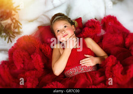 Pequeña princesa de invierno en una preciosa corona en vestido rojo se encuentra en la nieve artificial. Celebra la Navidad y Año Nuevo