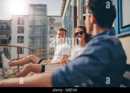 Foto de joven mujer sentada con sus amigos en la cafetería al aire libre. Grupo de jóvenes relajándose en un balcón.