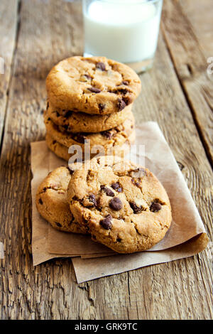 Las galletas con trocitos de chocolate con leche sobre papel y tabla de madera rústica