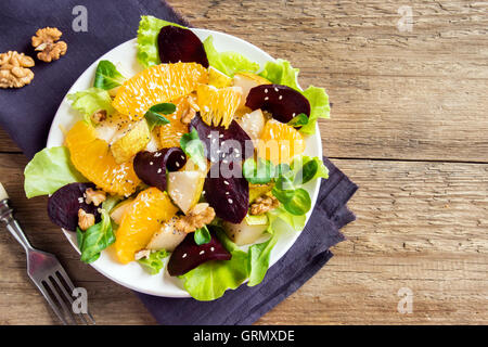 La remolacha y la naranja con ensalada de verdes, peras, nueces y semillas. Comida vegetariana saludable sobre fondo de madera con espacio de copia. Foto de stock