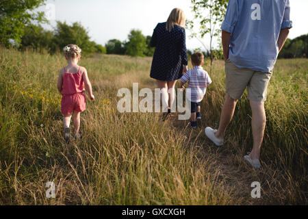 Vista trasera de la mitad de los padres adultos paseando en Meadow chico y chica Foto de stock