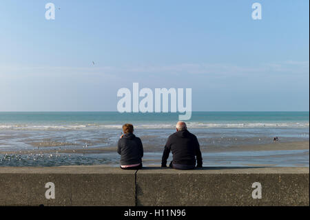Pareja Sentada sobre el mar con vistas a la playa de Muro vacío, Normandía, Francia Foto de stock