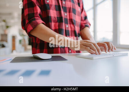 Cerca de manos del hombre escribiendo en el teclado del ordenador. Captura recortada empresario trabajando en un equipo mientras está de pie en su escritorio en de
