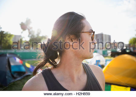 Retrato pensativo joven con moño de cabello y anteojos mirar lejos en el festival de música de verano camping