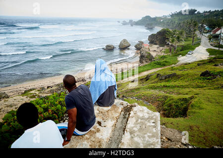 Barbados Betsabé costa atlántica ver ocean los hombres locales boys sentado mirando al mar tranquilo descansando sentado en piedra elevada hayas Foto de stock