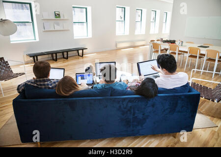 Vista trasera de la gente de negocios con ordenadores portátiles en un sofá en la oficina creativa Foto de stock