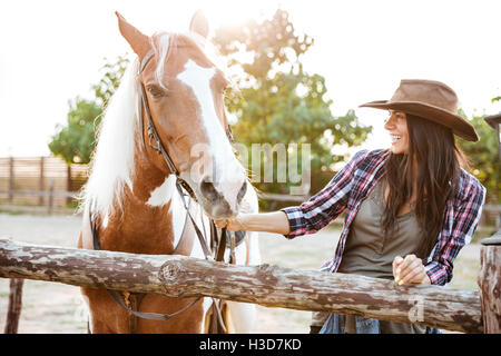 Sonriente joven atractivo cowgirl caminar a caballo en la granja