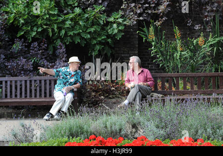 Dos señores ancianos sentados conversando en una banca del parque, mientras que dos niños Juego Pokemon junto a ellos. Foto de stock