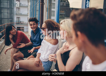 Grupo multirracial de amigos sentados en el balcón. Los jóvenes relajarse al aire libre en la terraza.