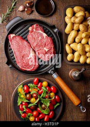 Filete de carne cruda en la parrilla, patatas, tomates y especias, vista superior, sobre la mesa de madera