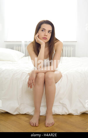 Joven mujer se sienta cuidadosamente en el borde de su cama, Foto de stock
