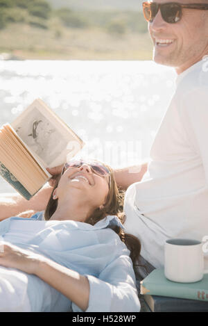 Hombre y mujer recostado sobre un embarcadero, leyendo un libro.