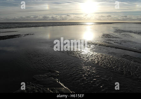 Cruzando el canal de agua de mar de la playa de arena en marea baja extensión al sol blanco horizonte hundiéndose estratocúmulos nubes, Fairhaven, Lytham, REINO UNIDO Foto de stock