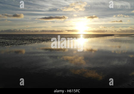 Puesta de sol blanco debajo de grises nubes estratocúmulos reflejando en un canal de agua de mar cruzando la arena de la playa en marea baja, Fairhaven, REINO UNIDO Foto de stock