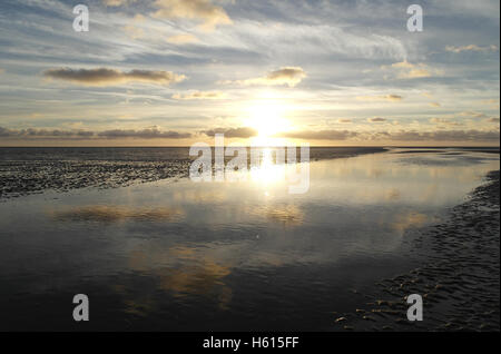 Puesta de sol blanco debajo de grises pequeñas nubes estratocúmulos reflejando en un canal de agua de mar en la playa de arena, en marea baja Fairhaven, REINO UNIDO Foto de stock