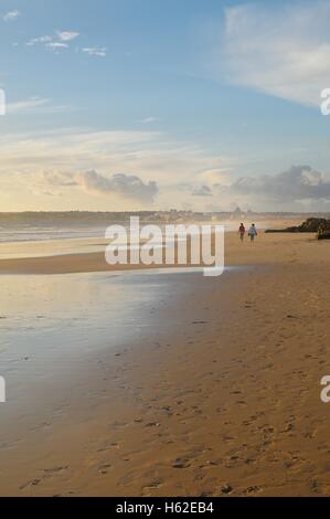 Cifras distantes caminar sobre la playa en la dorada luz del atardecer Foto de stock