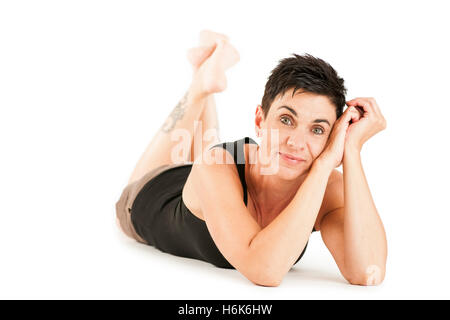 Vista completa del cuerpo de pelo negro de una mujer de mediana edad buscando descalzo en shorts y top negro en el vientre recostado contra un blanco volver Foto de stock