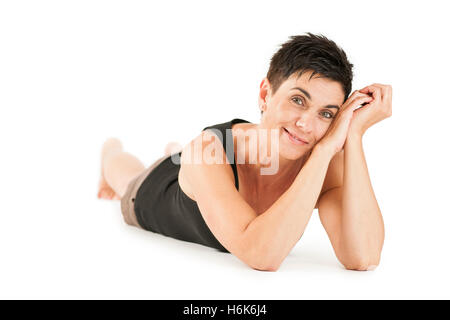 Vista completa del cuerpo de pelo negro de una mujer de mediana edad buscando descalzo en shorts y top negro en el vientre recostado contra un blanco volver Foto de stock