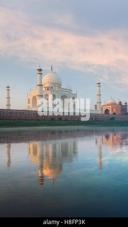 El majestuoso Taj Mahal de mármol rojo y naranja brillante mezquita bellamente reflejado en el suave río Jamuna en amanecer Foto de stock