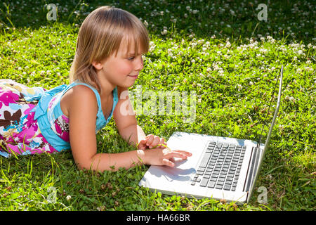 Niña con ordenador portátil en un jardín de verano Foto de stock