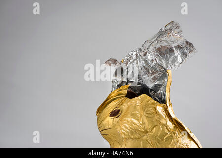 Conejito de Pascua de chocolate, envuelto en oro y plata brillante papel de aluminio, parcialmente erosionado, lámina rasgué abierto en la parte superior Foto de stock
