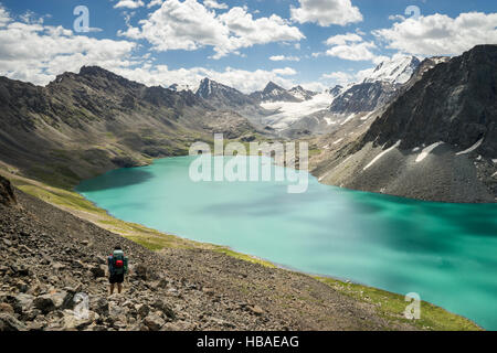 Un montañero hombre detiene su sendero de trekking para observar las montañas nevadas y Ala Lago Kul, Kirguistán Foto de stock