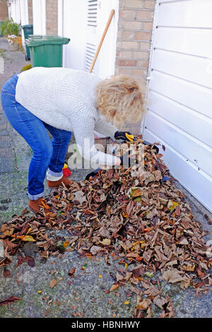 Mujer barriendo y limpiando el caído hojas de otoño desde su entrada en Brighton Reino Unido