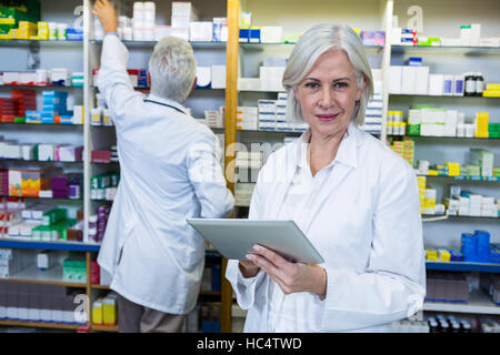 Farmacéutico utilizando tablet digital y co-trabajador controlar los medicamentos Foto de stock