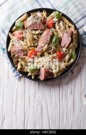 Penne pasta con carne, queso parmesano, tomate y salsa pesto en una placa vertical vista superior Foto de stock