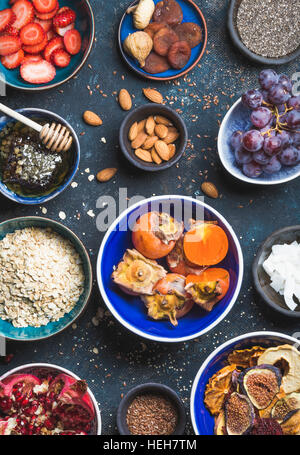 Ingredientes en recipientes para el desayuno saludable sobre fondo azul oscuro, vista superior. Frutas frescas y secas, semillas de chia, avena, las nueces, la miel. Limpie el comer, Foto de stock