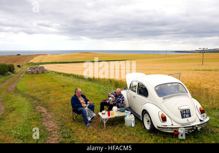 Dos holandeses tienen un picnic junto a sus VW beetle en un campo cerca de St Abbs, Berwickshire, Scottish Borders, Scotland, Reino Unido Foto de stock