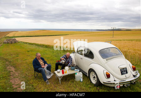 Dos holandeses tienen un picnic junto a sus VW beetle en un campo cerca de St Abbs, Berwickshire, Scottish Borders, Scotland, Reino Unido Foto de stock