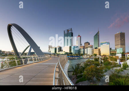 A lo largo del crepúsculo ver Elizabeth Quay puente peatonal de la ciudad más allá, Perth, Australia Occidental, Australia Foto de stock
