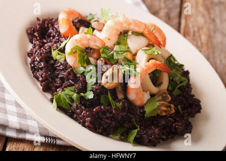 Arroz negro salvaje con gambas, calamares, mejillones y vieiras de cerca en un plato sobre la mesa. Horizontal