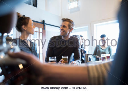 Pareja sonriente hablando y bebiendo cerveza en el bar en la sala de degustación de cerveza