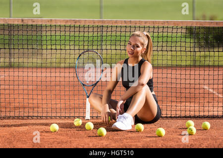 Mujer joven sentado delante de net con raqueta y pelotas de tenis, pista de tenis, Suiza Foto de stock
