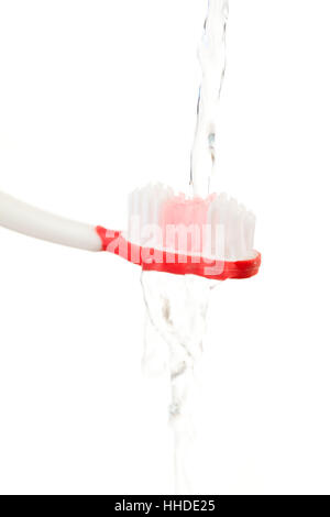 El agua que fluye en un cepillo de dientes rojo contra el fondo blanco. Foto de stock
