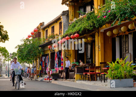 Pareja joven bicicleta pasado atractiva cafetería casas en Hoi An, Vietnam, Indochina, en el sudeste de Asia Foto de stock
