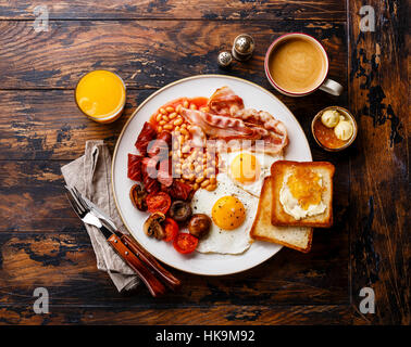 Completo desayuno inglés con huevos fritos, salchichas, tocino, frijoles, tostadas y café sobre fondo de madera