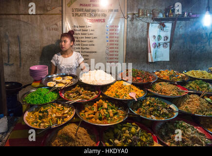 En Luang Prabang, Laos - 15 de mayo de 2015: Una joven mujer laosiana vende comida a los turistas en un puesto en el mercado en el mercado nocturno de Luang Prabang.