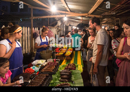 En Luang Prabang, Laos - 15 de mayo de 2015: Los turistas compran alimentos desde un puesto en el mercado en el mercado nocturno de Luang Prabang.