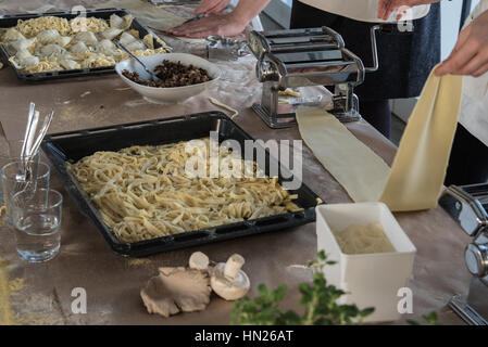 Persona que opera una máquina de pasta con pastas recién hechas y otros alimentos en la mesa Foto de stock