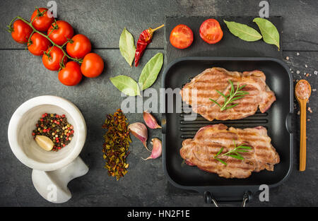 Bistec con las especias y los tomates cocinados en la parrilla sobre una mesa oscura vista superior