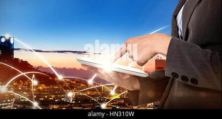 Sección media de la empresaria mediante digital tableta contra edificios iluminados en la ciudad contra el cielo Foto de stock