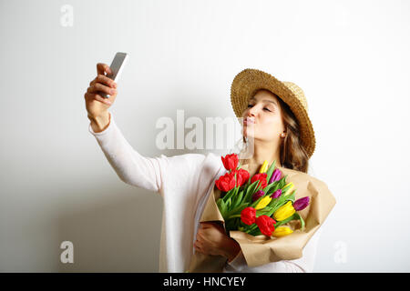 Mujer joven con besar los labios sosteniendo un ramo de flores en su mano, y hace la foto selfie Foto de stock