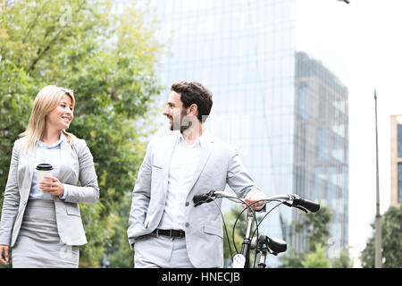 Empresarios con bicicleta y copa desechable conversando mientras camina al aire libre Foto de stock