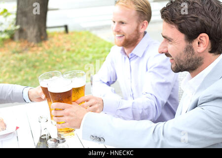 Los empresarios de tostar los vasos de cerveza con el colega en el restaurante al aire libre Foto de stock