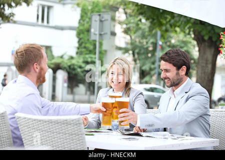 Felices empresarios tostar los vasos de cerveza en el restaurante al aire libre Foto de stock