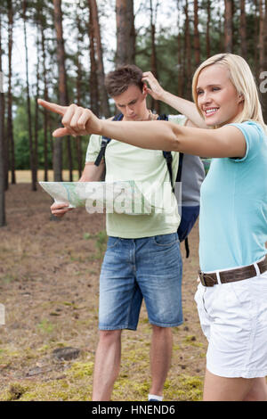 Mujer joven apuntando hacia fuera con el confundido hombre sujetando el mapa del bosque Foto de stock